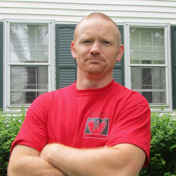 Tom Breslawski is standing in front of a house looking at the camera with his arms crossed.