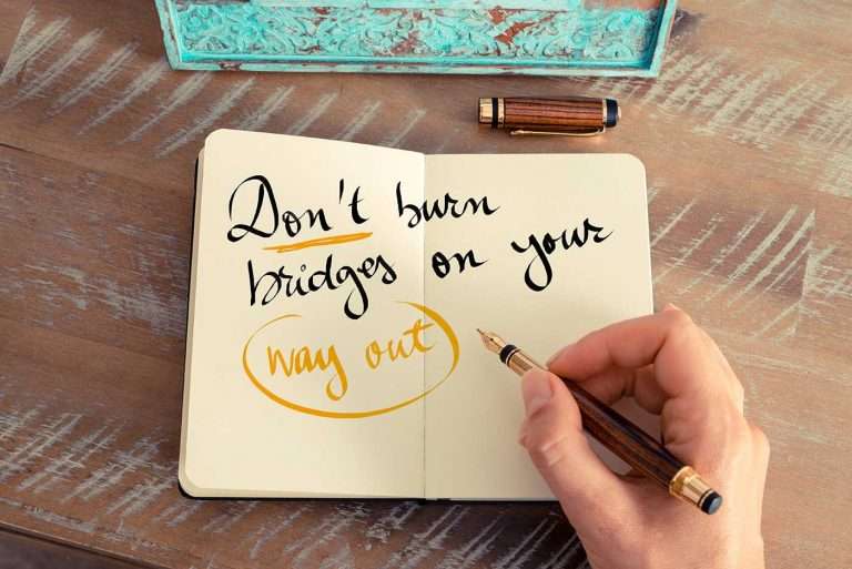 A person hand writing a note with a fountain pen on a notebook. The written text reads: Don't Burn Bridges On Your Way Out.