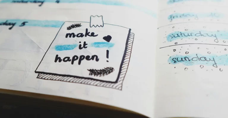 Closeup of a notebook page with a hand-drawn post-it note that says Make It Happen!