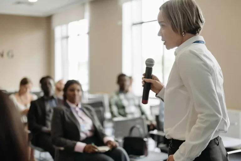 A businesswoman speaks into a microphone to a seated audience.