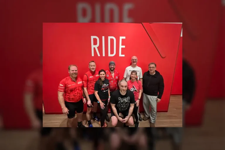 A group of bicyclists standing and kneeling in front of a large red backdrop with the word Ride in all capital letters.