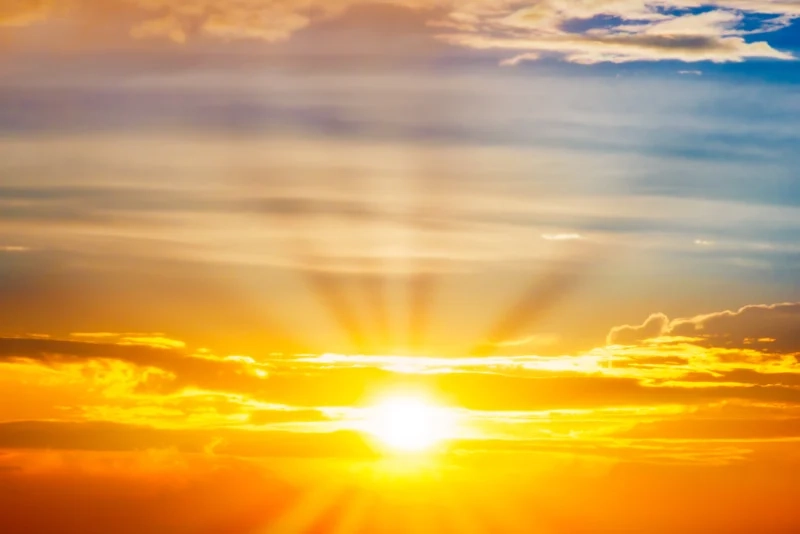Sun rising through clouds with sun rays emanating outward.