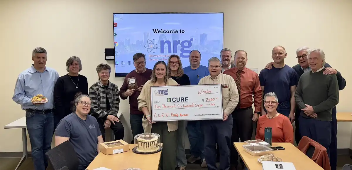 NRG members pose for a group photo with Holly Dutcher, presenting the Executive Director of CURE Childhood Cancer Association, with a check of the proceeds from its annual Dessert Auction.