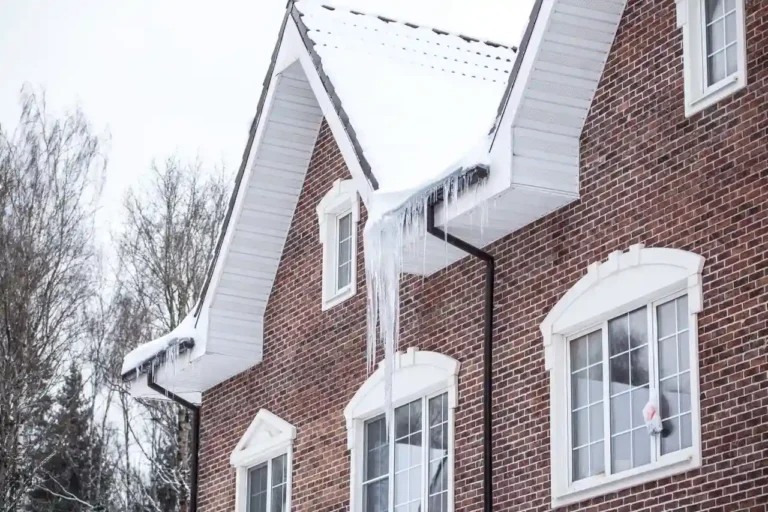 A brick house with snow-covered roof and ice damming above the gutter and large icicles hanging down.