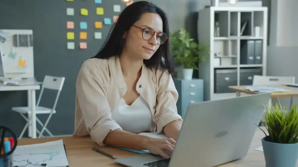 Focused woman typing on a laptop in a modern office setting.